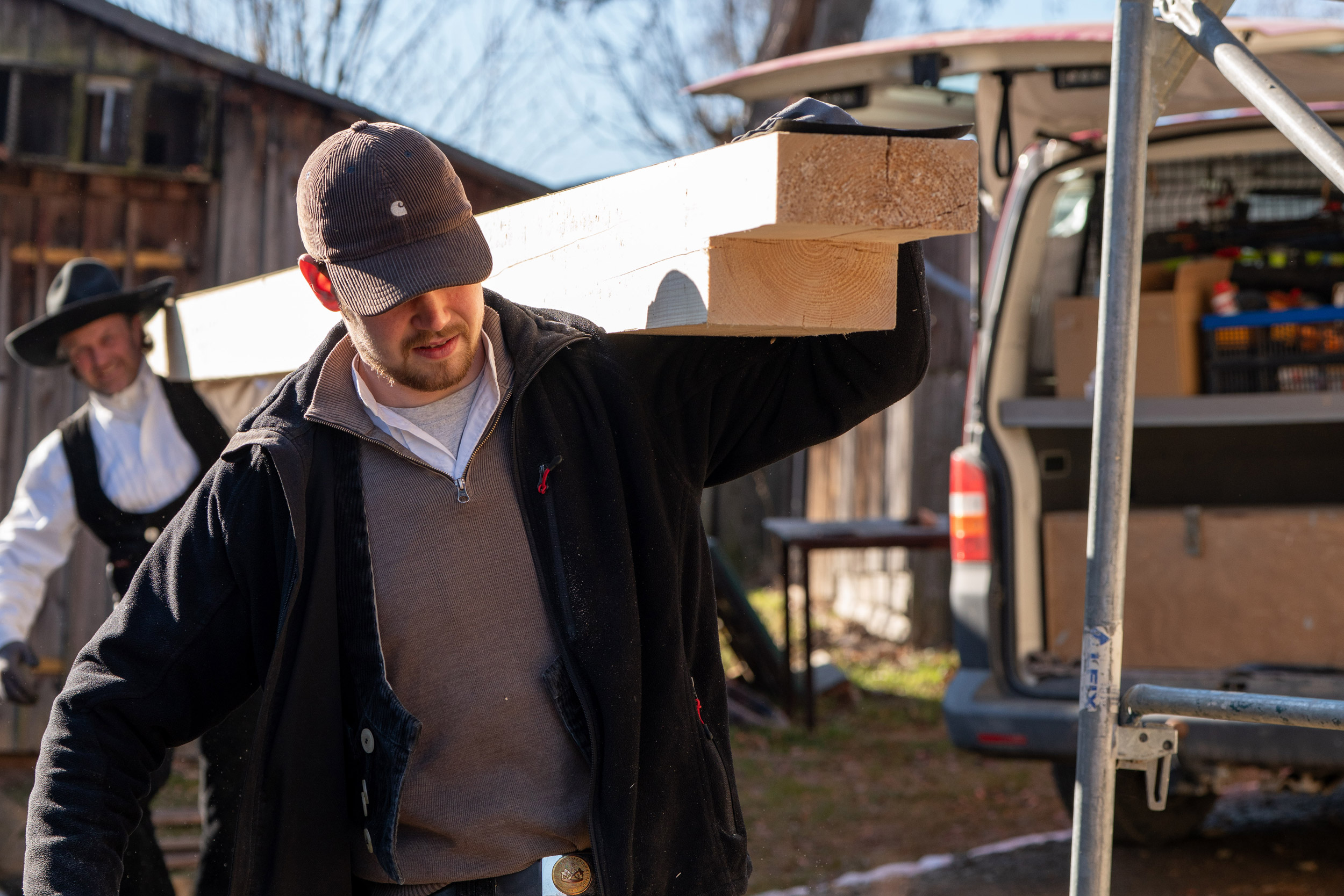zwei Zimmerleute tragen gemeinsam Holzbalken auf die Baustelle